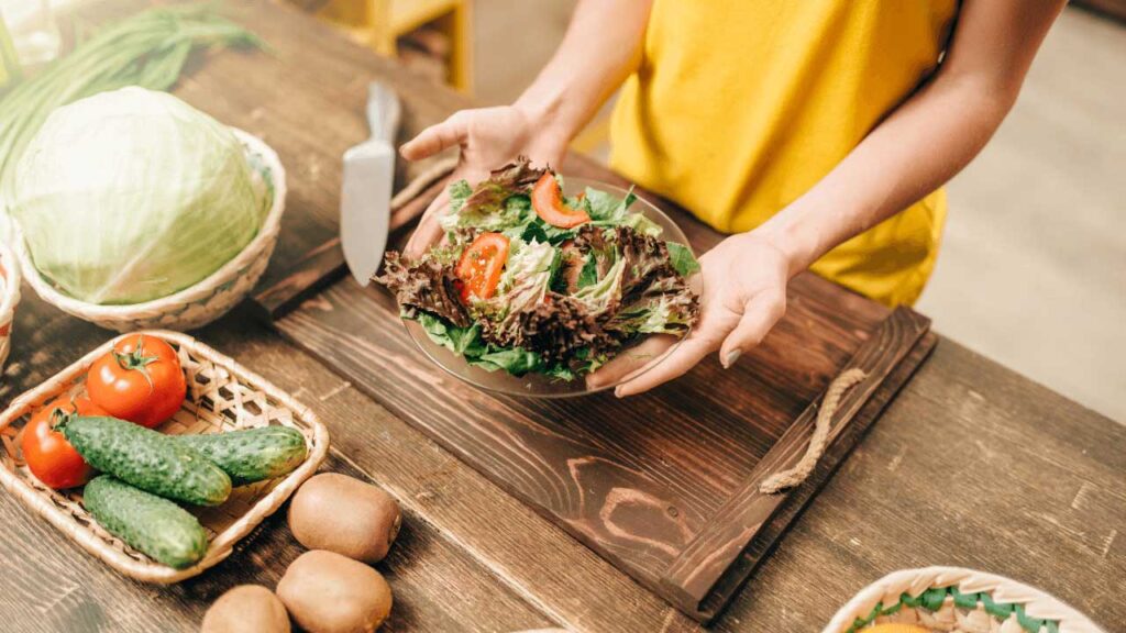 Personne posant une assiette de salade sur une table en bois