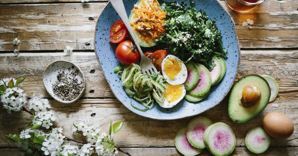 Assiette colorée de légumes, avocat et œuf sur une table en bois