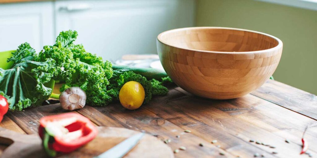 Bol en bois vide entouré de légumes frais sur une table de cuisine